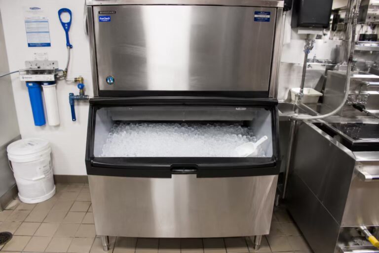 Hoshizaki commercial ice machine above a storage bin beside water filters in a kitchen